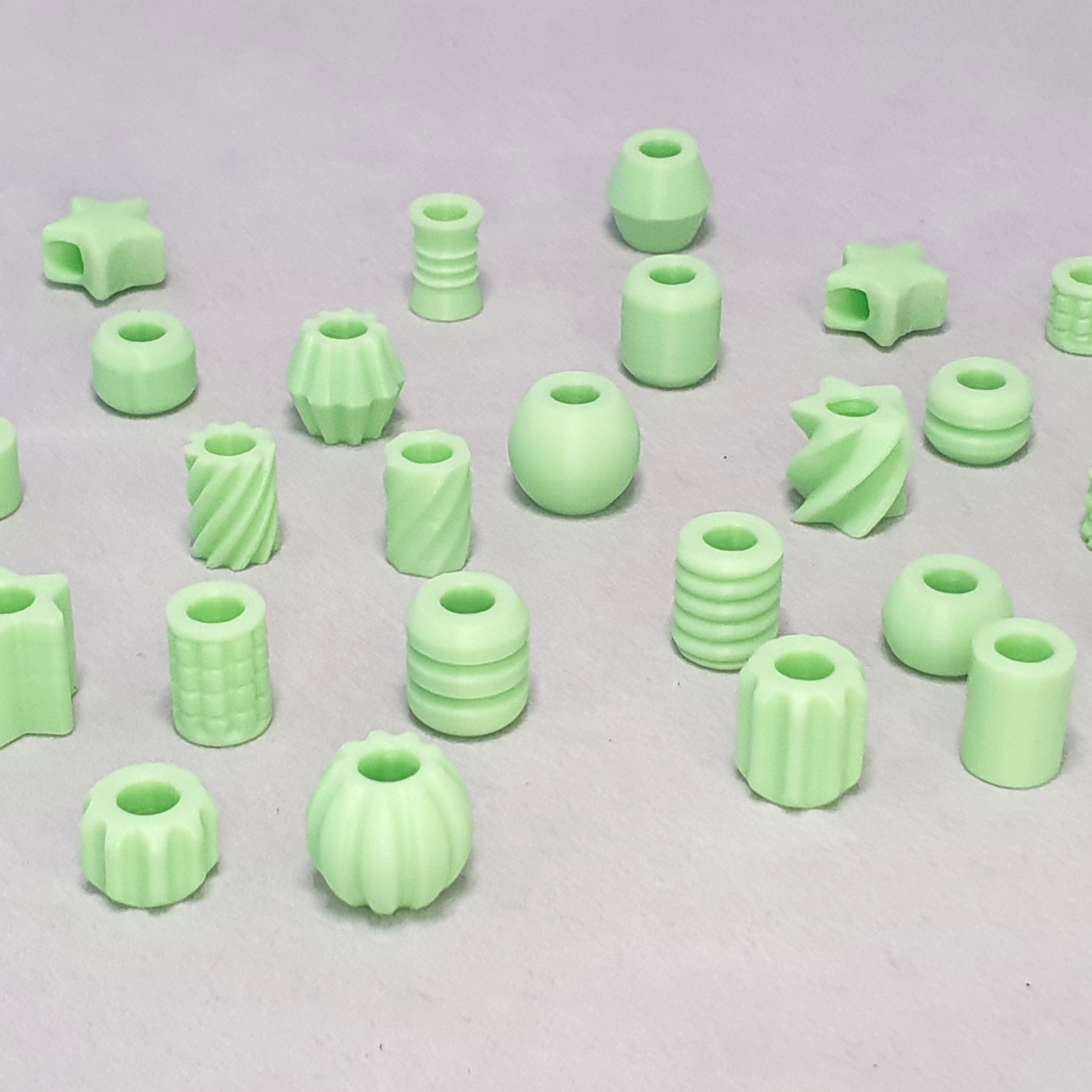Assorted glow in the dark 3D printed dreadlock beads in mint green, variety of shapes including ribbed, spiral, star and sphere