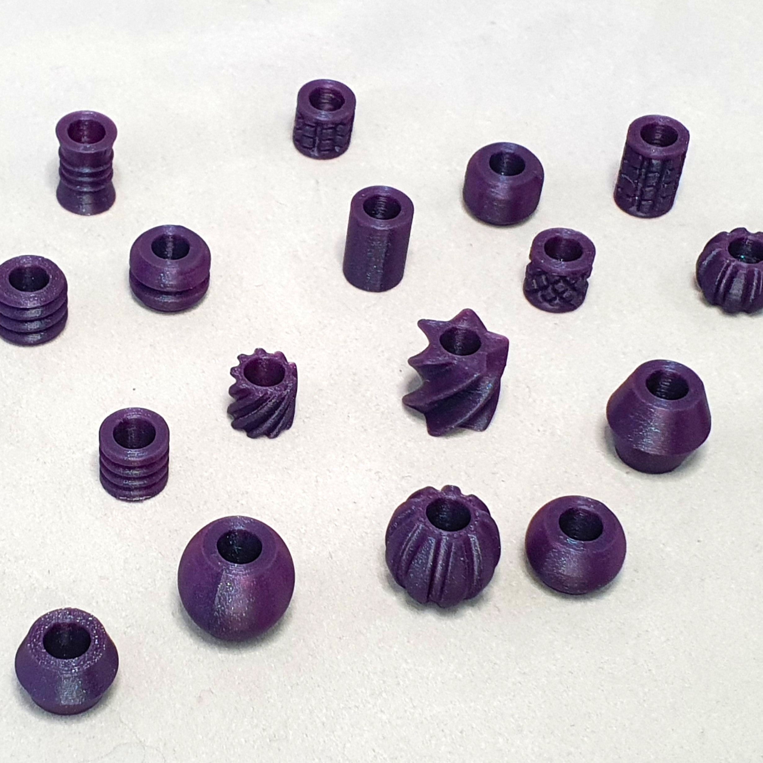 Assorted sparkly purple 3D printed dreadlock beads in a variety of shapes including ribbed cylinders, spirals, stars and spheres