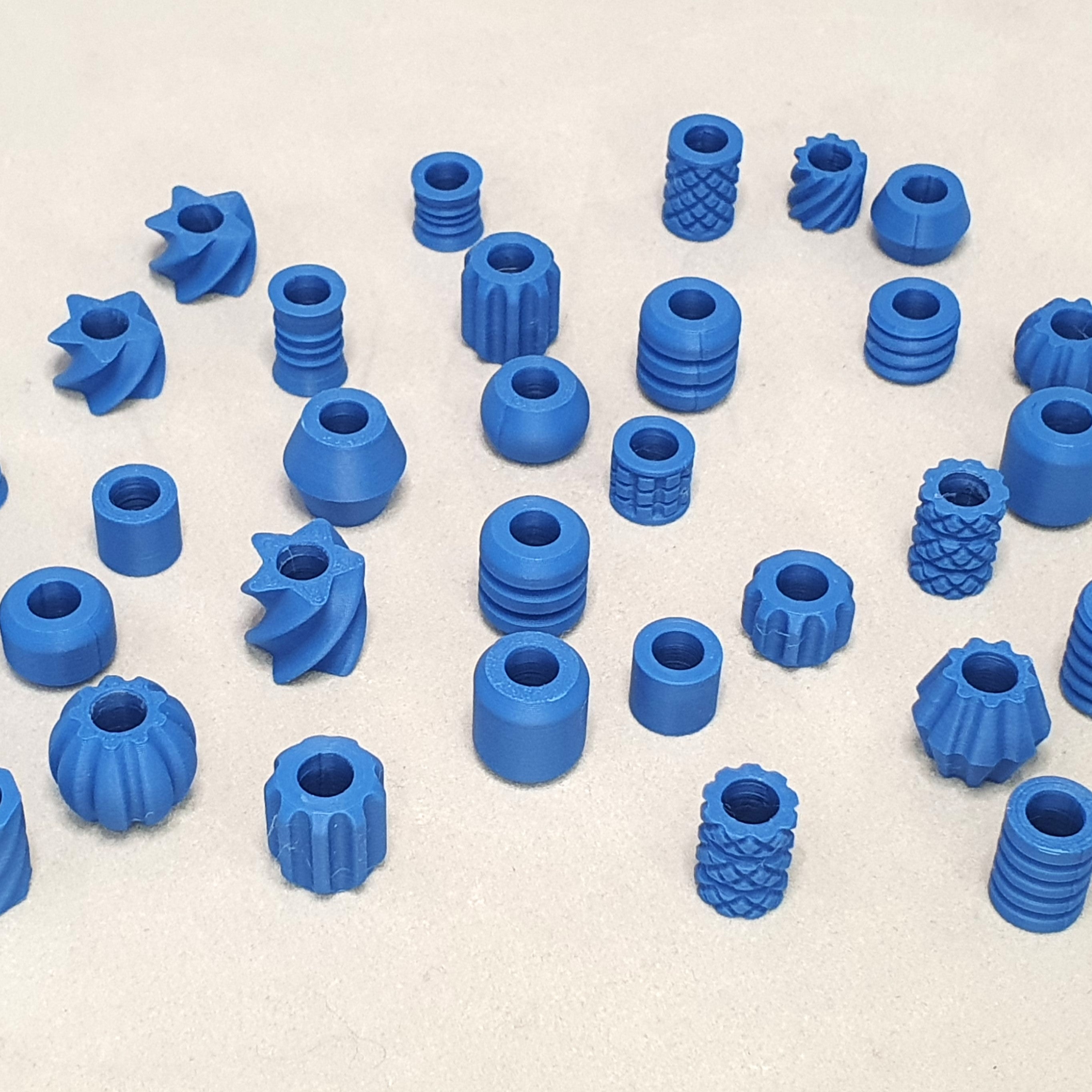 Assorted matte blue 3D printed dreadlock beads in a variety of shapes including ribbed cylinders, pineapple texture, spirals, stars and spheres